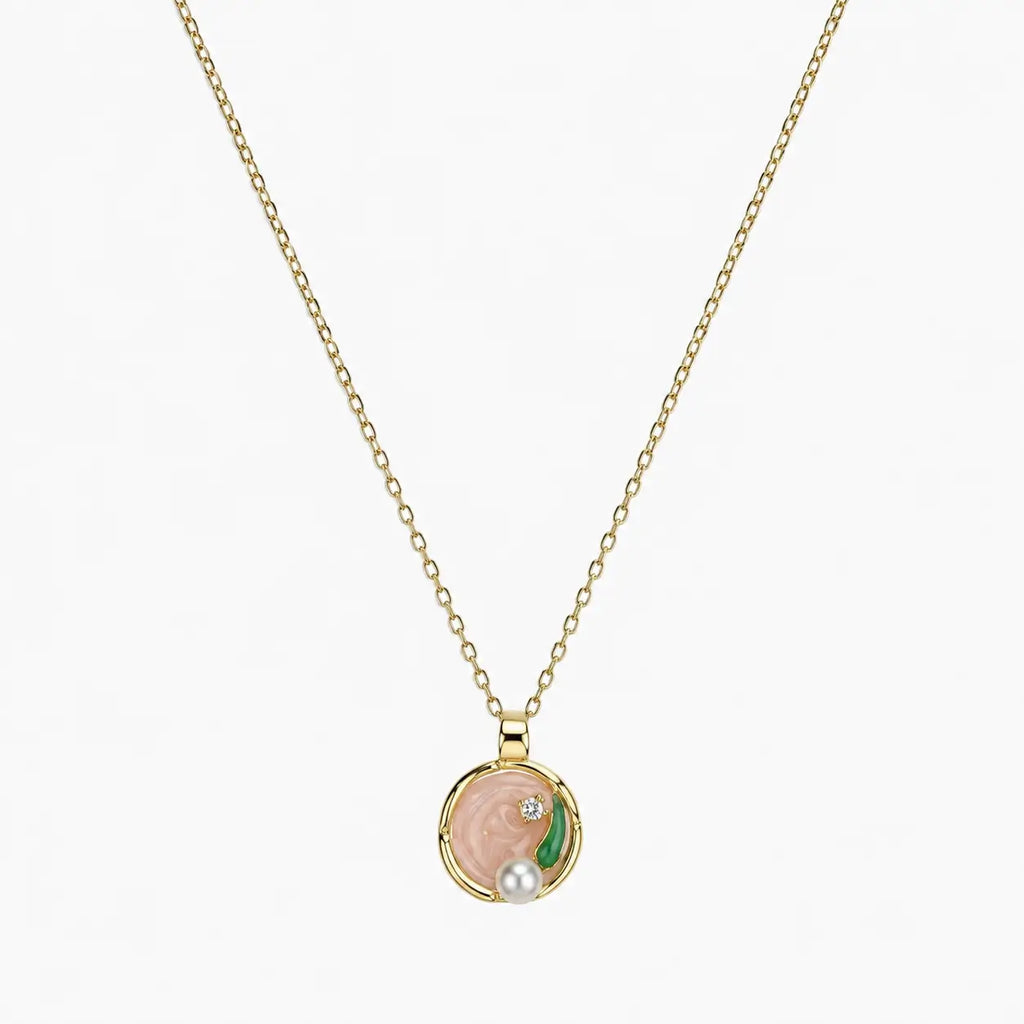 Close-up of a gold-tone pendant necklace with pink swirl centre, green leaf, clear stone and pearl-like accent.