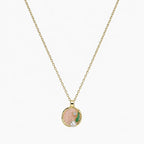 Close-up of a gold-tone pendant necklace with pink swirl centre, green leaf, clear stone and pearl-like accent.