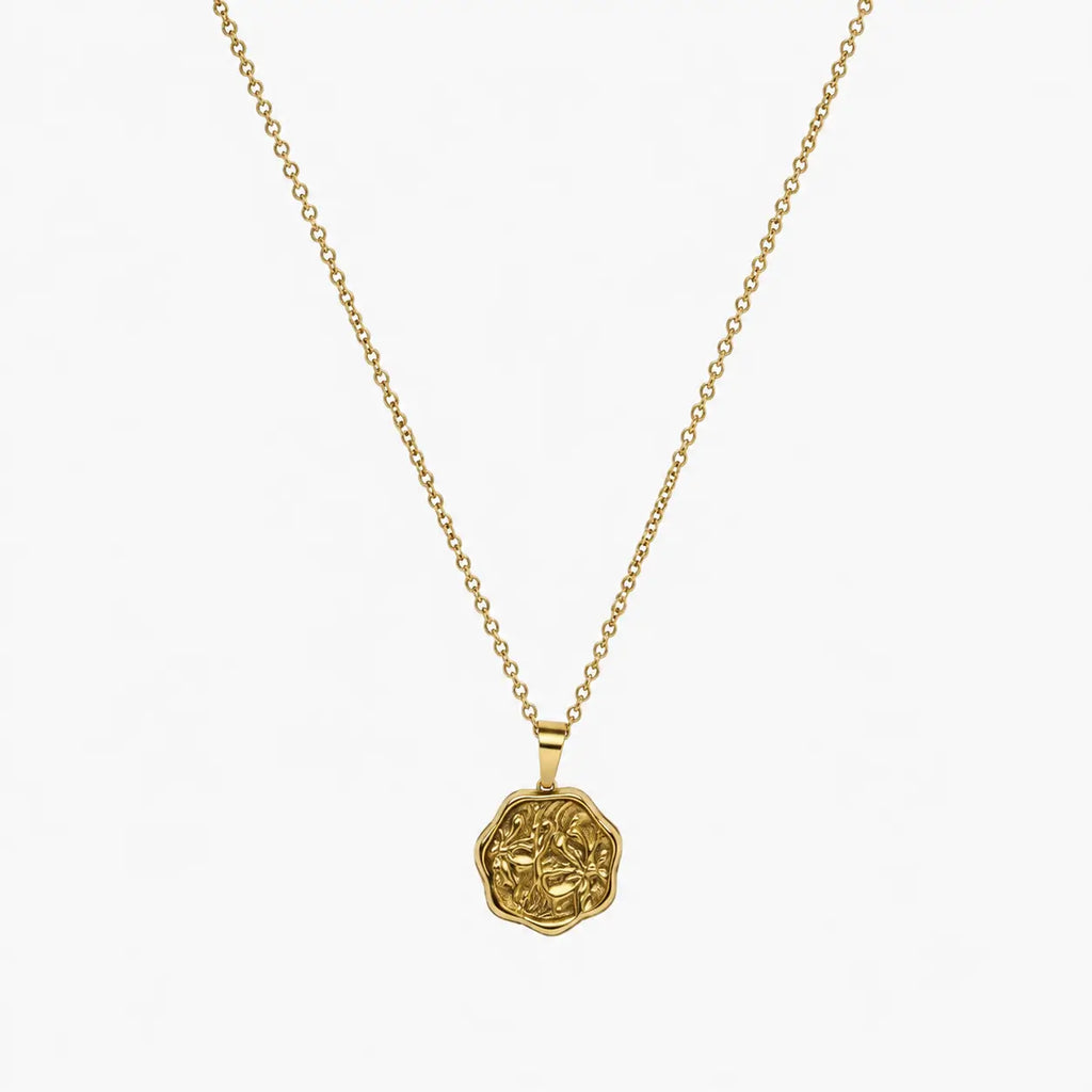 Close-up of a gold-tone artificial pendant necklace with an irregular embossed floral coin charm.