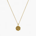 Close-up of a gold-tone artificial pendant necklace with an irregular embossed floral coin charm.