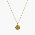 Close-up of a gold-tone artificial pendant necklace with an irregular embossed floral coin charm.