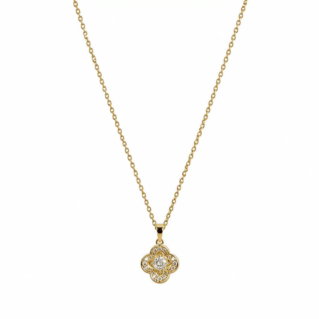  Close-up of a gold-tone pendant necklace with four-lobed clover shape and clear centre stone.