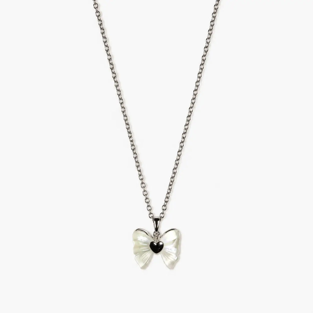 Close-up of a silver-tone pendant necklace for girls with a pearlescent bow and glossy black heart centre.