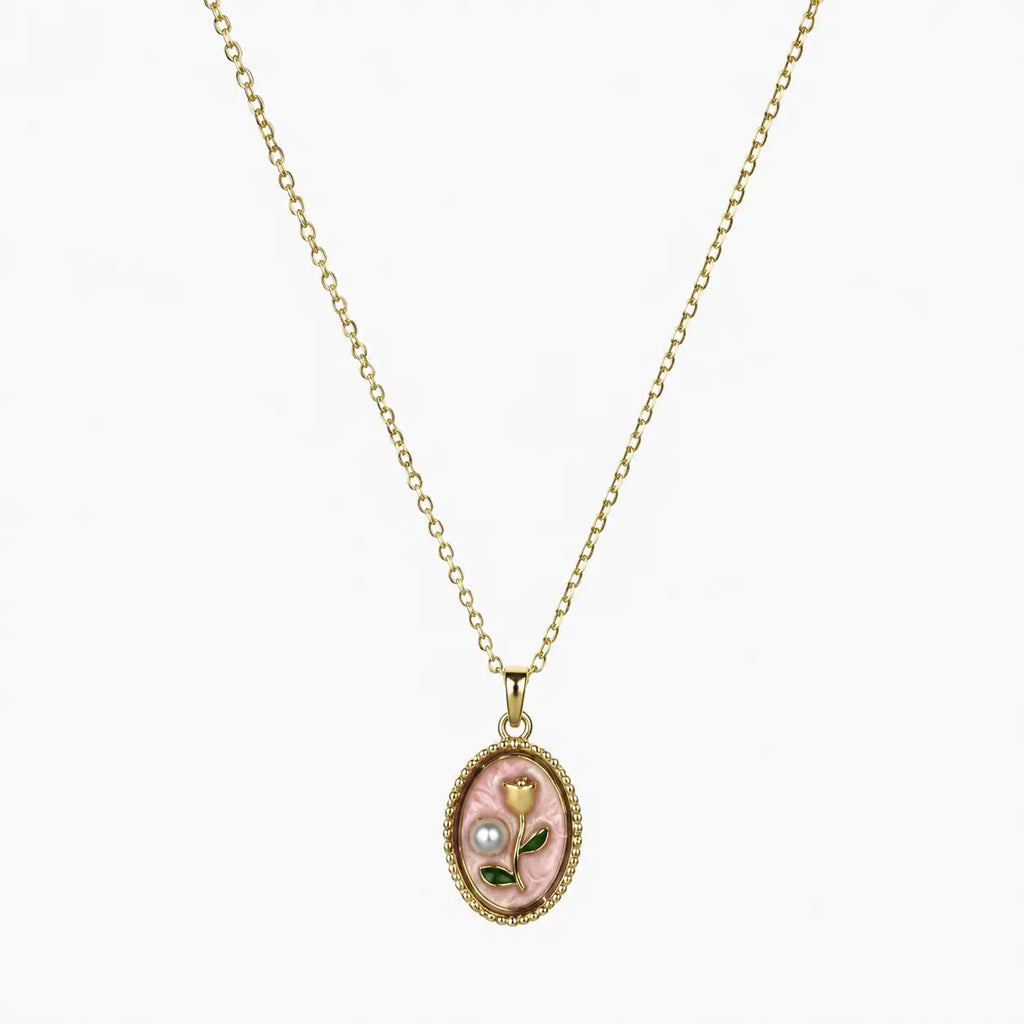 Close-up of a gold-tone pendant necklace with pink oval floral charm, green leaves and pearl-like accent.