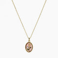 Close-up of a gold-tone pendant necklace with pink oval floral charm, green leaves and pearl-like accent.