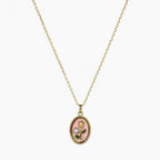 Close-up of a gold-tone pendant necklace with pink oval floral charm, green leaves and pearl-like accent.