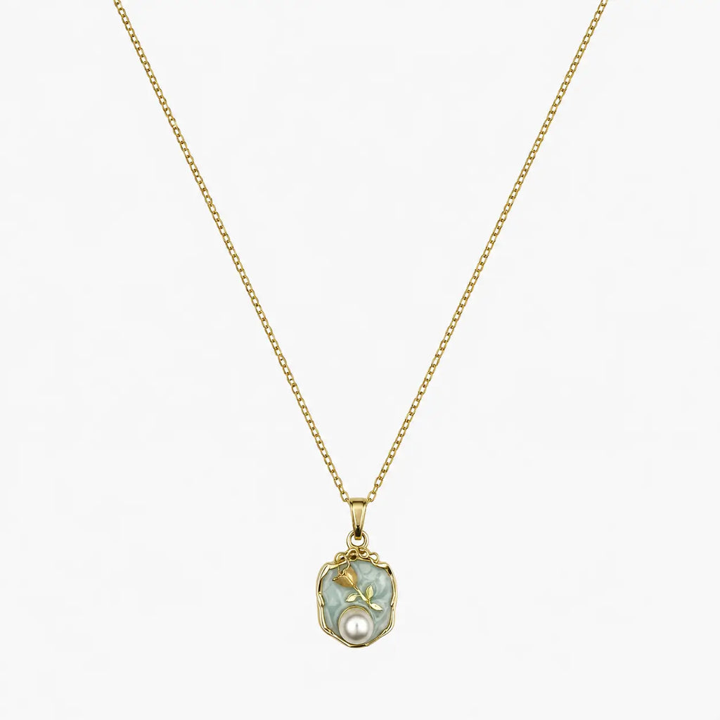 Close-up of a gold-tone pendant necklace with a soft green floral medallion and pearl-like accent.