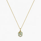 Close-up of a gold-tone pendant necklace with a soft green floral medallion and pearl-like accent.